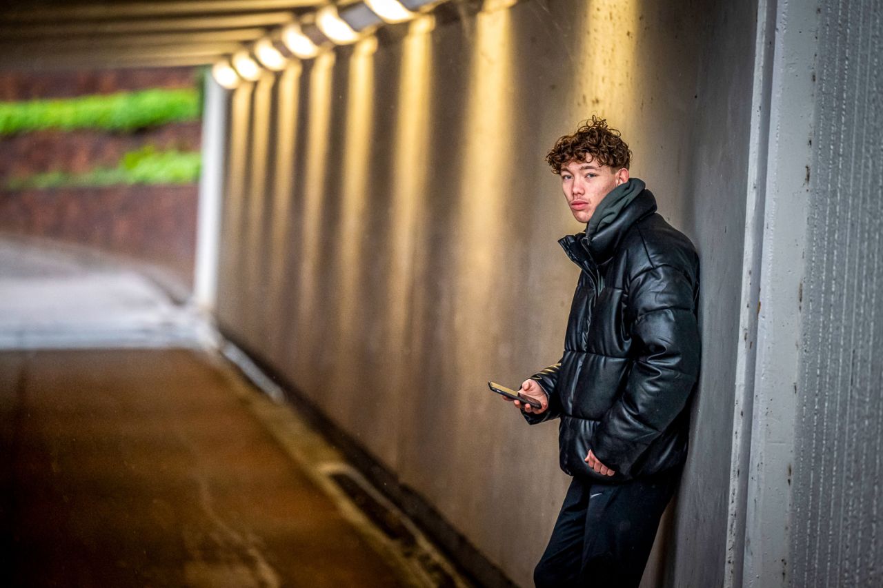 Afbeelding: een jongen die onder een tunnel staat en op zijn telefoon zit.